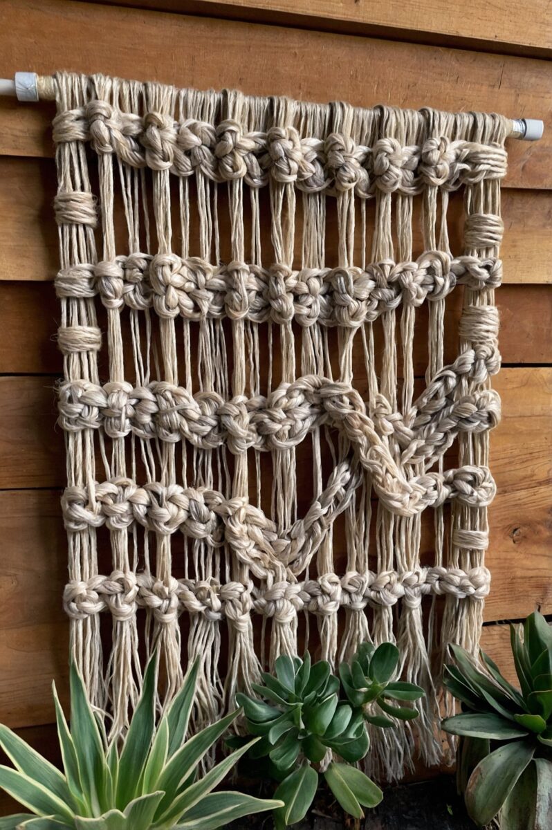 Handmade macramé wall hanging with heart design and flower knots in natural cotton rope on wooden fence
