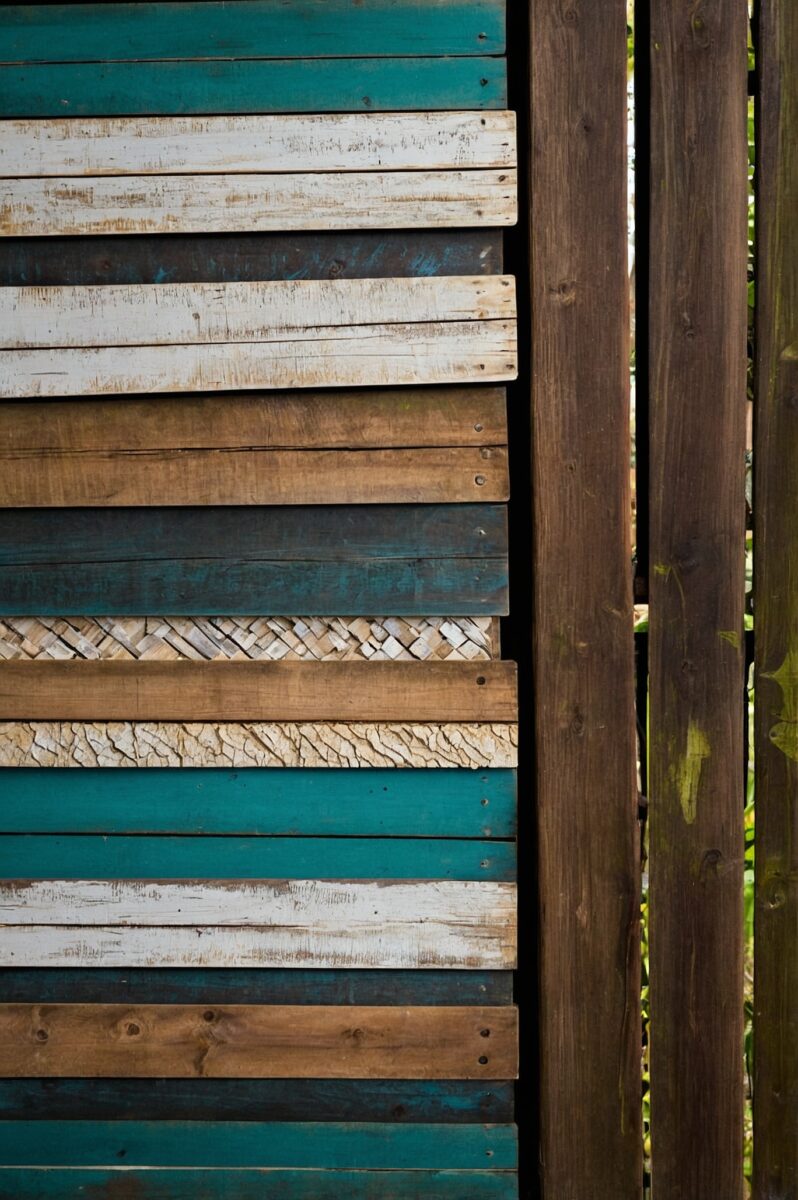 Rustic wall made of mixed reclaimed wood planks in teal, white, and natural brown tones with woven bamboo accent strip