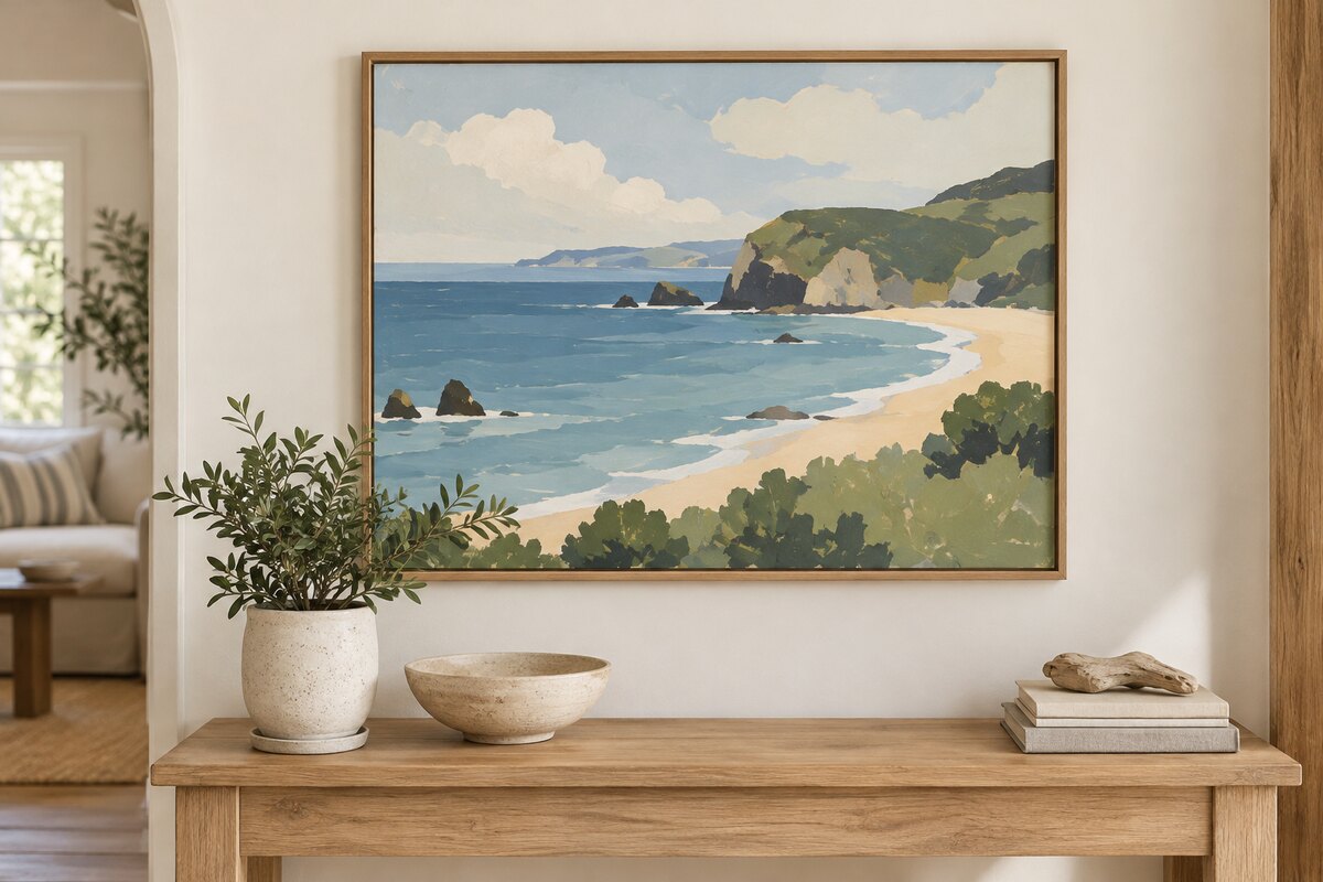 A hand-painted canvas of a coastal landscape from a photo, framed and hung above a console table with a small plant