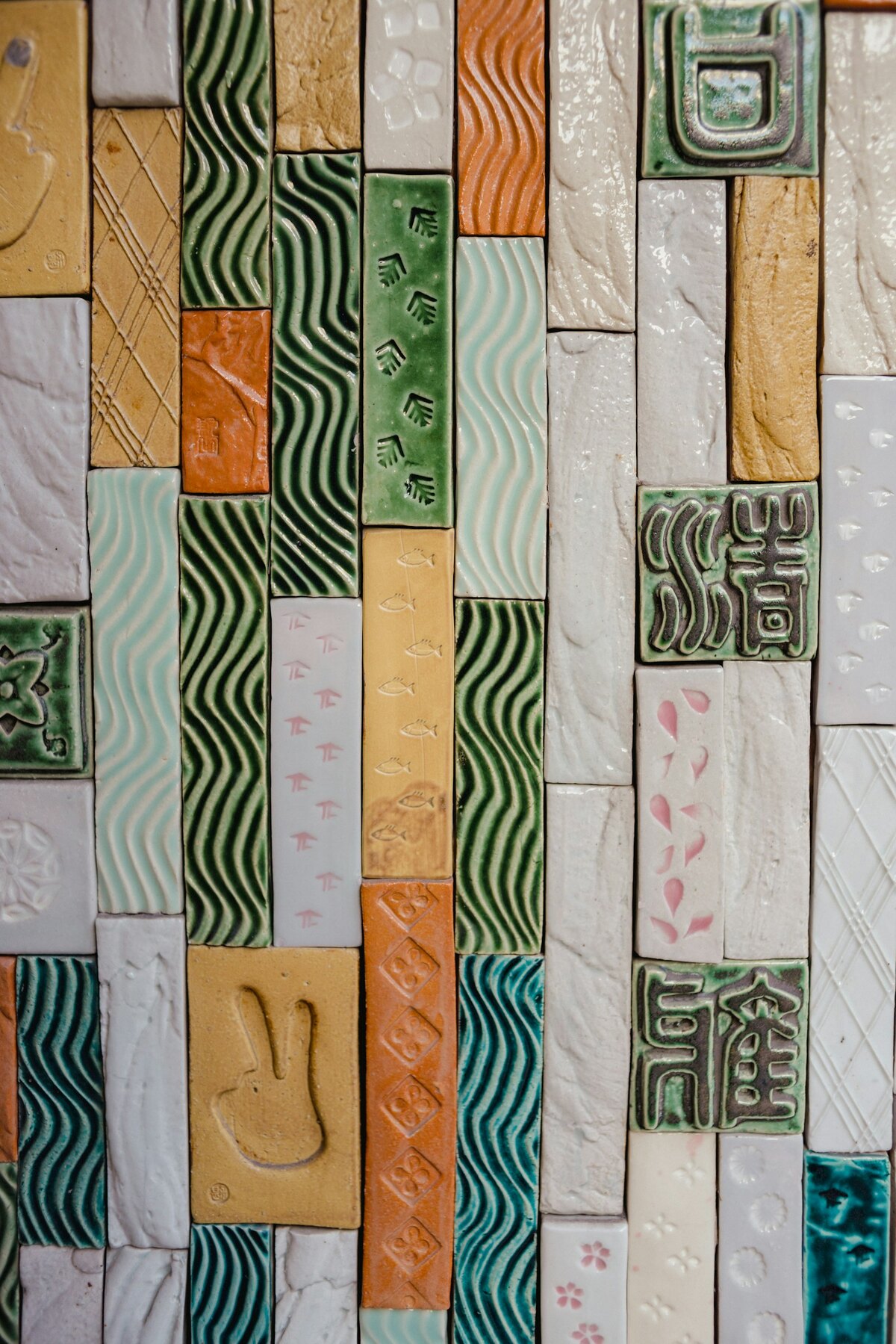 A wall of handmade relief tiles with pressed patterns, glazed in greens, creams and terracotta