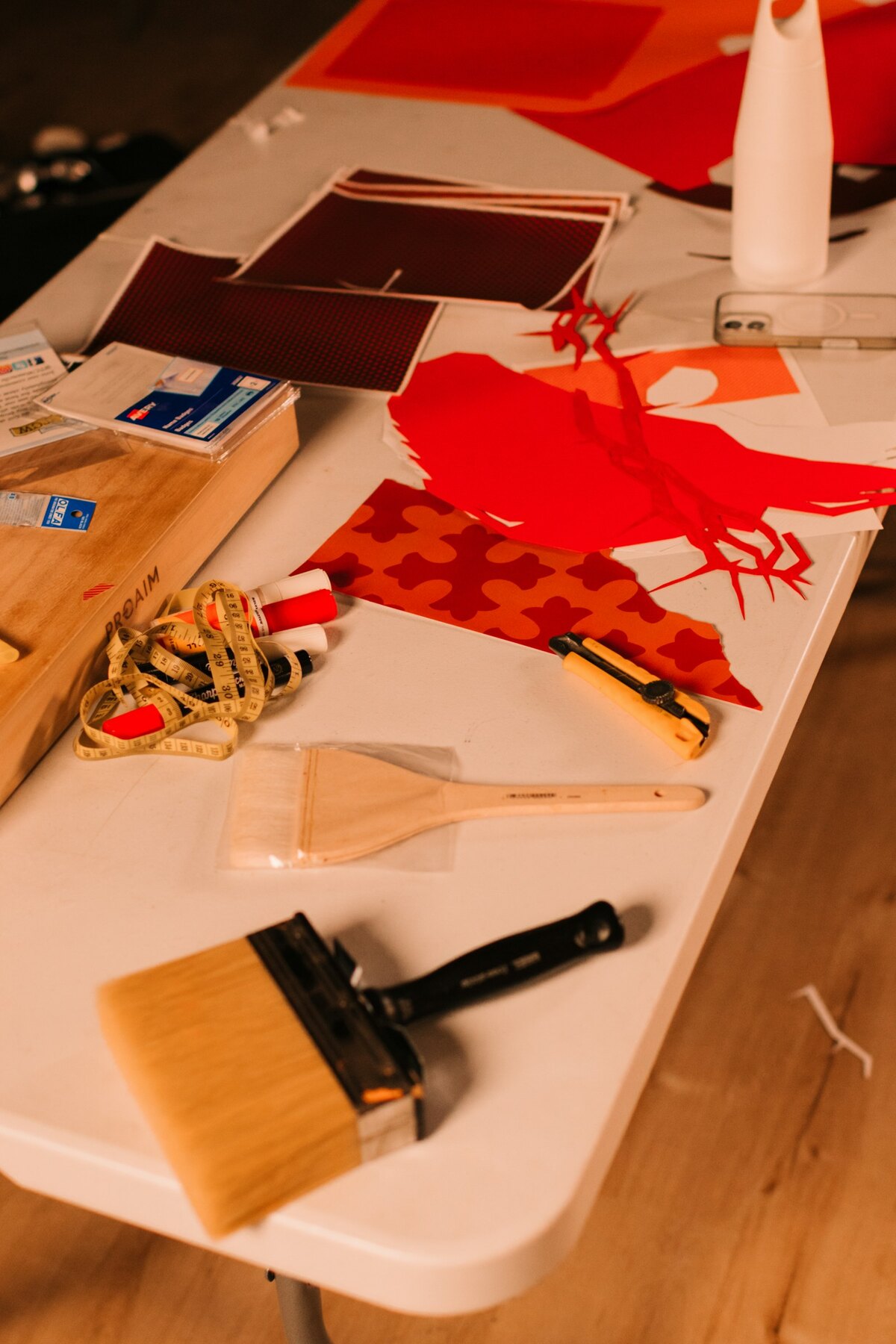 Craft supplies spread across a white table: paper cutouts, a wide brush, tape and twine