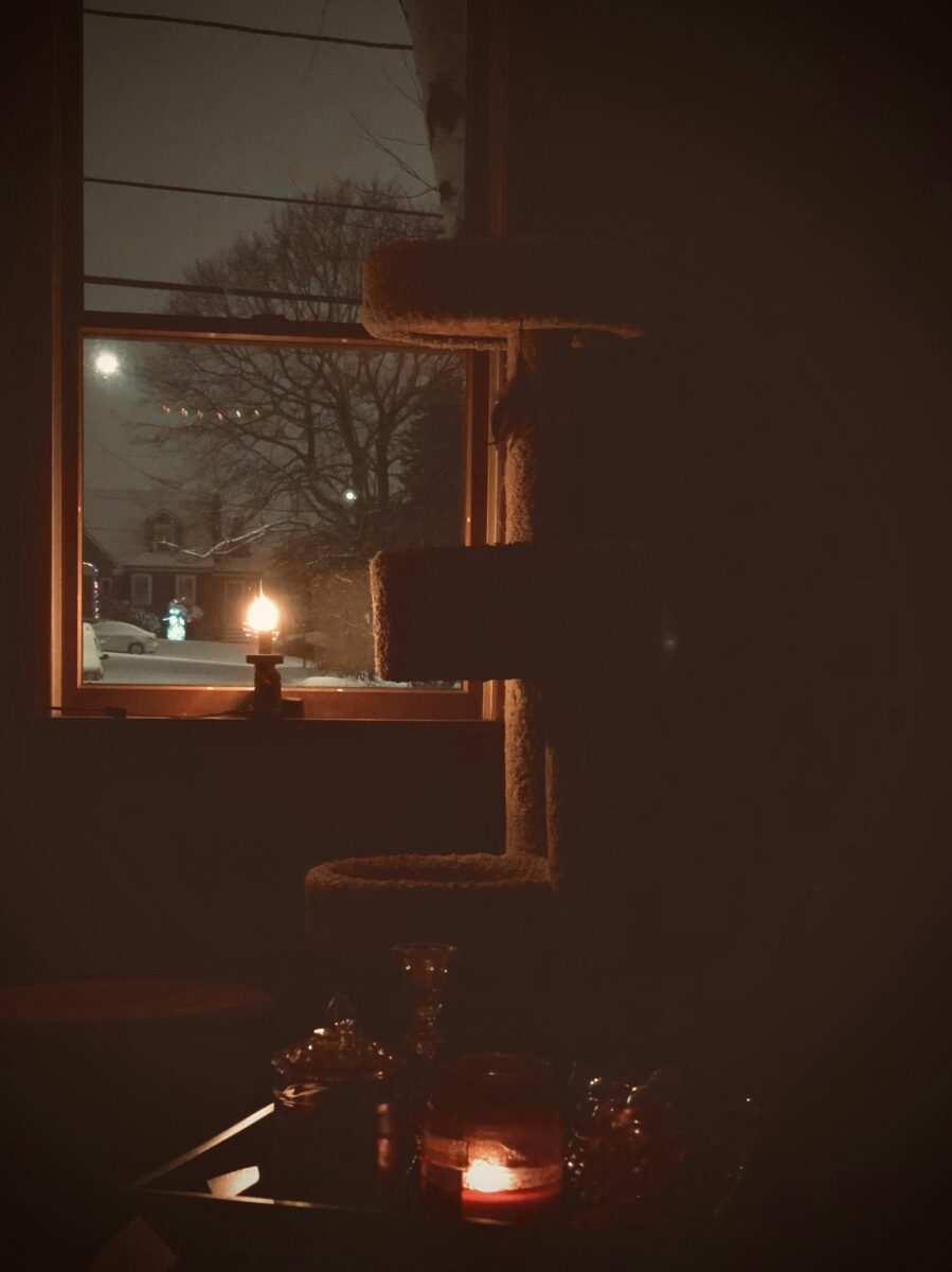 One candle glowing in a window at night, a snowy street and a lit lamp post outside