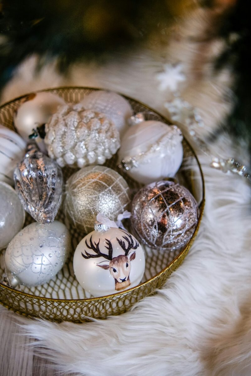 A gold wire bowl filled with white and silver Christmas ornaments on a white faux fur throw
