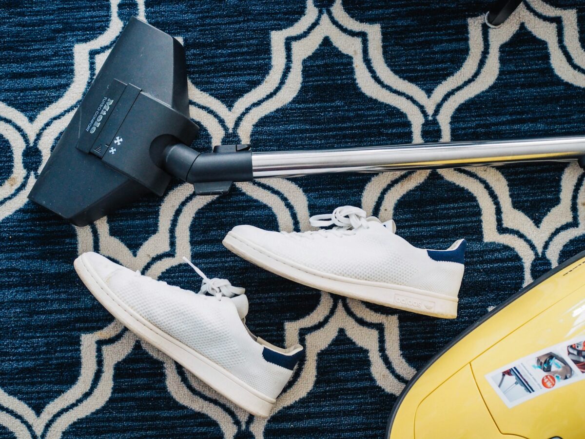 A vacuum cleaner and a pair of white sneakers on a flat navy and cream trellis rug