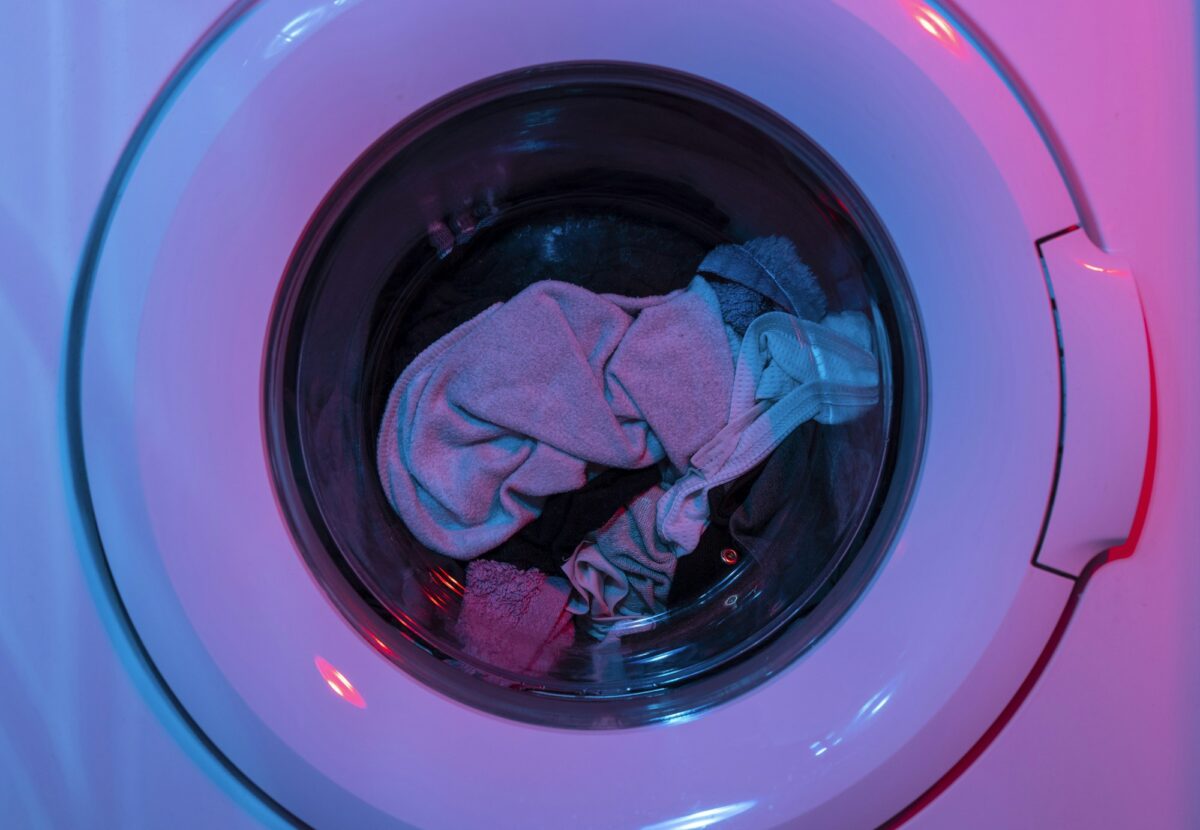 A load of laundry inside the drum of a front-load washing machine, lit pink and blue