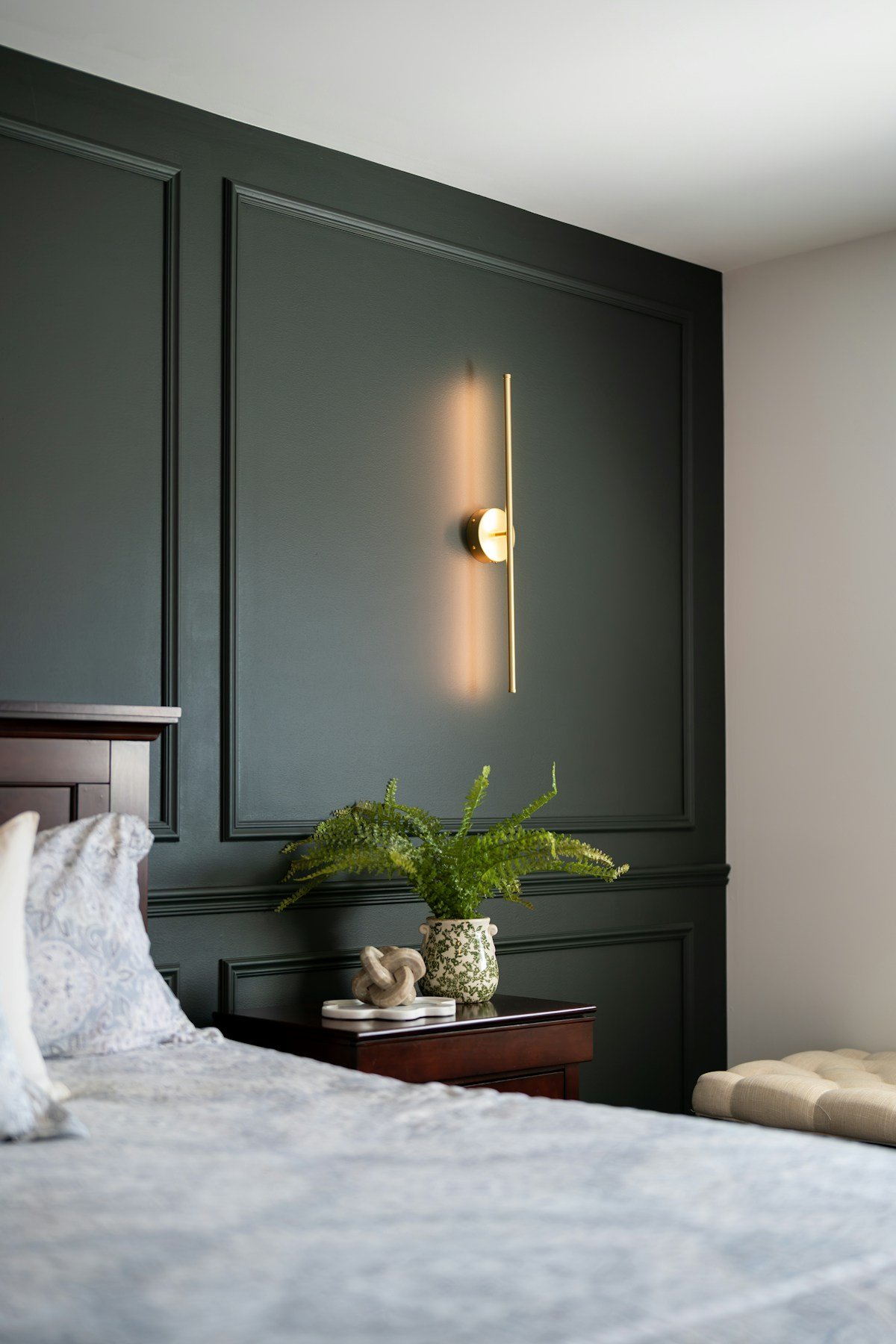 Bedroom with one dark green paneled accent wall behind the bed, a brass wall sconce and a light side wall