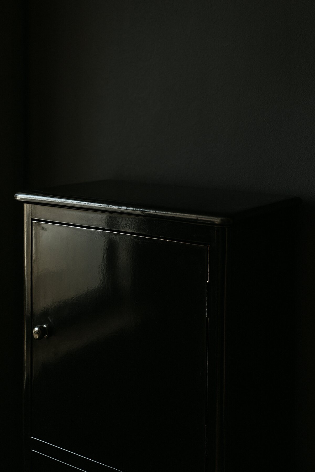 A glossy black lacquered cabinet pushed close to a near-black wall, its outline almost lost in the dark