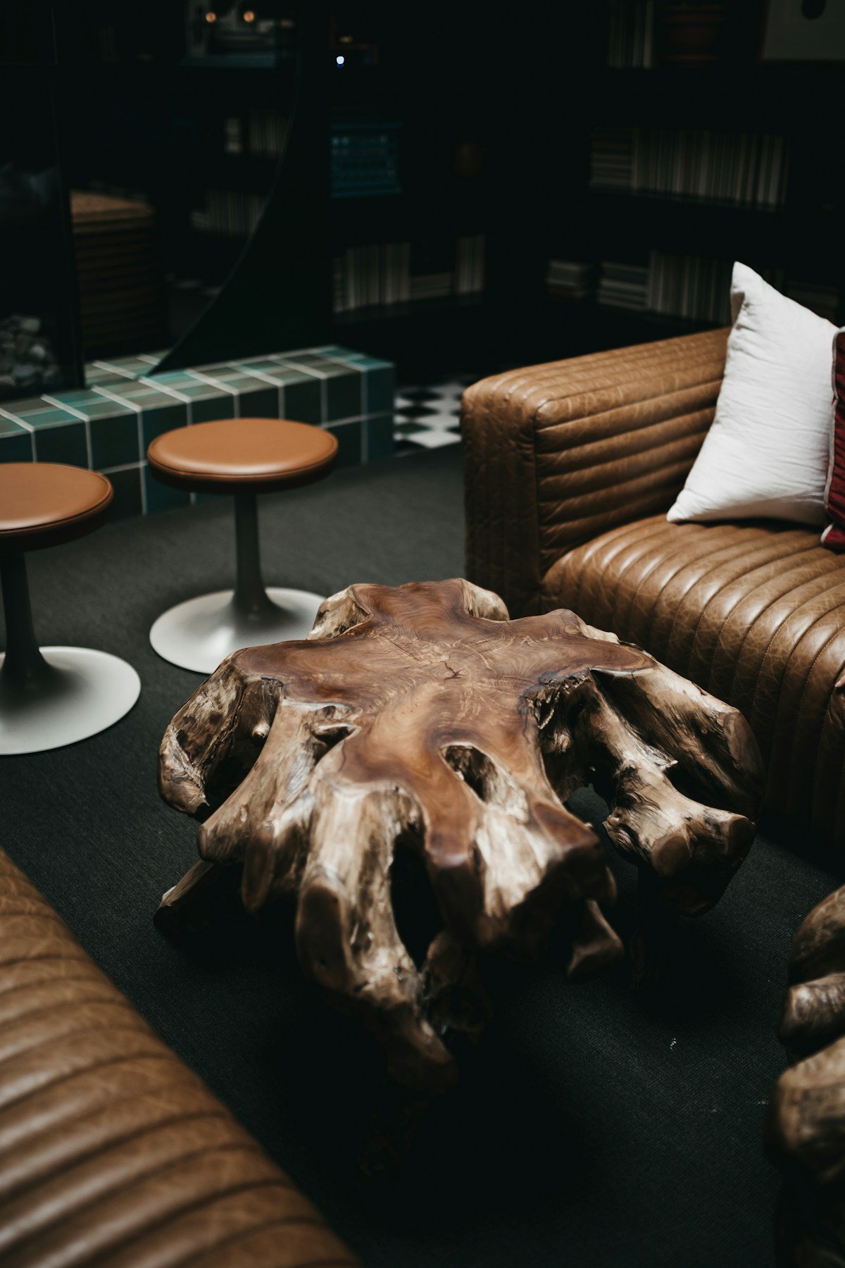 Two cognac leather sofas around a chunky wood root coffee table in a dark, moody living room
