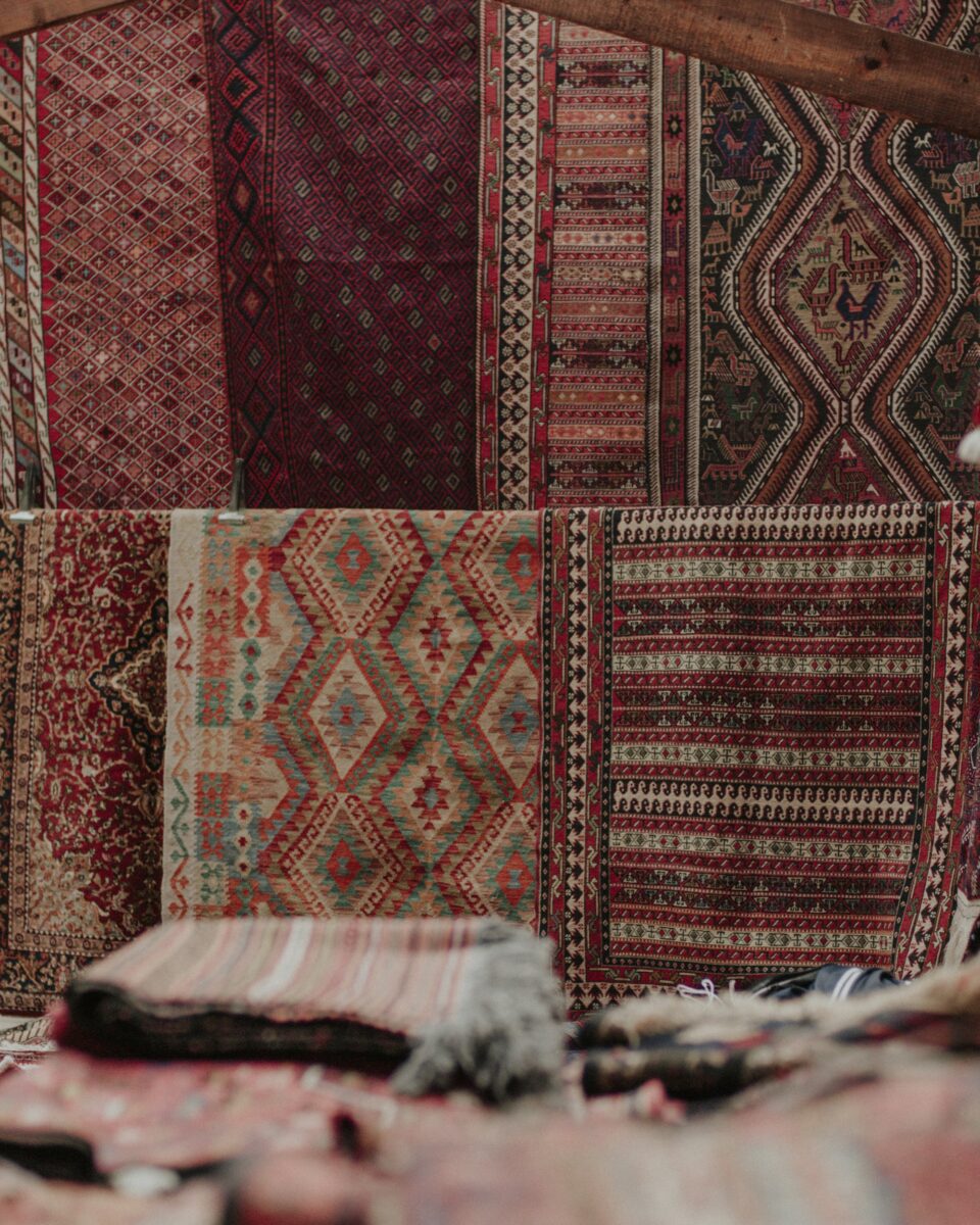A rug dealer's wall of hanging rugs and kilims in diamond lattice, stripes, medallions with small animal figures and red florals